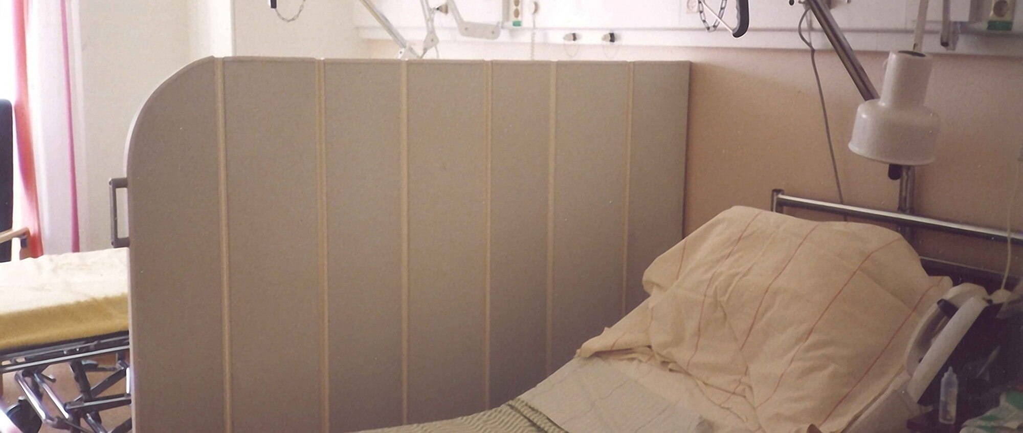 Ancien paravent pliant Silentia beige installé près d’un lit dans une chambre de patient, photo d’archive.