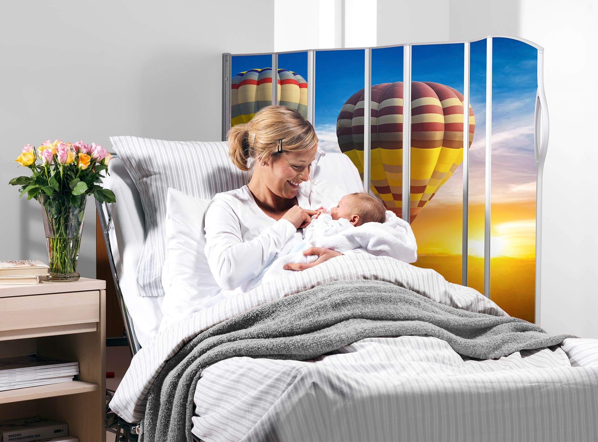 Mother holding her baby in bed beside a Silentia screen printed with the Hot air balloon PhotoPanels™ image.