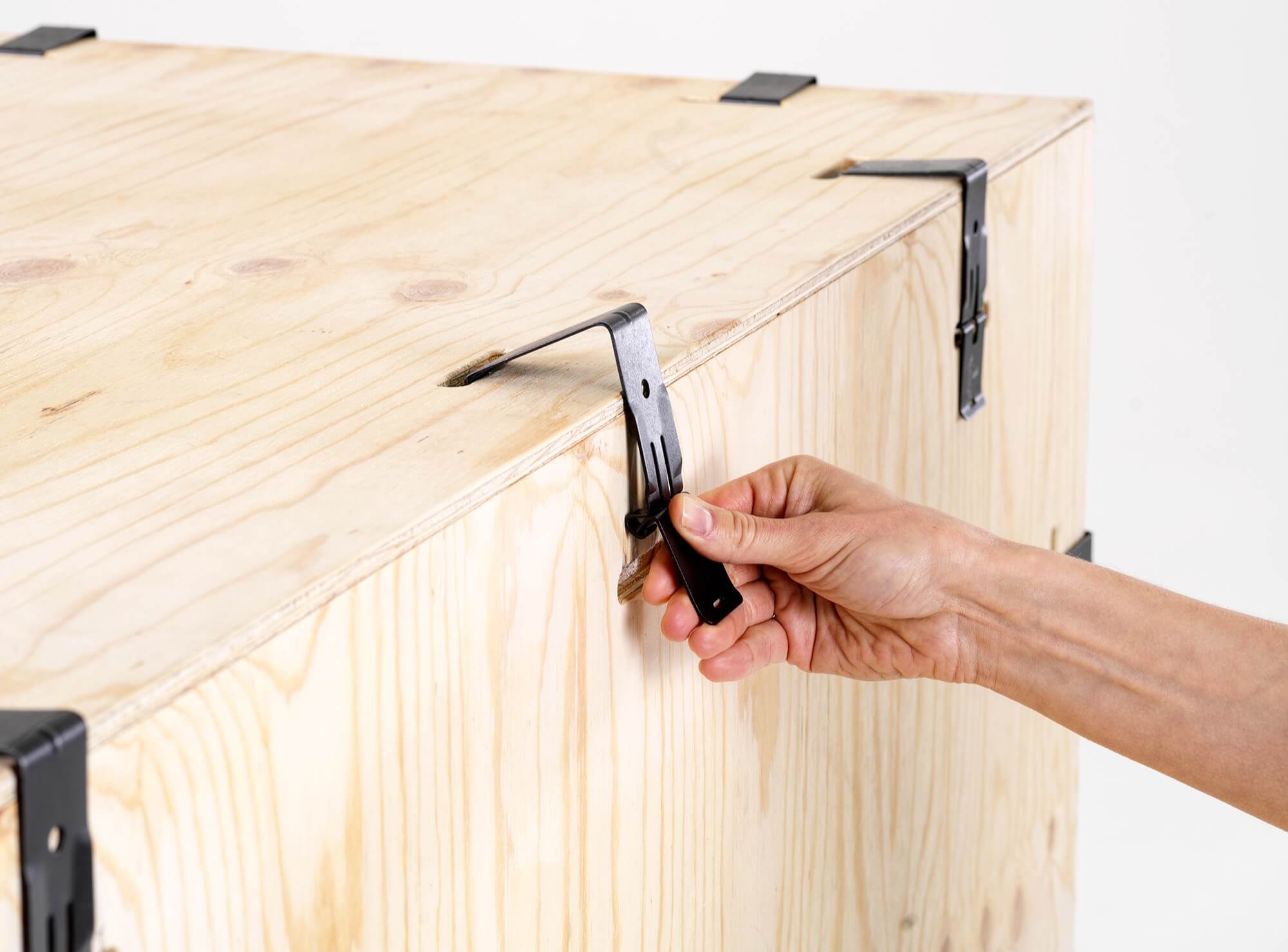 Handen maken de metalen clips los die een houten Silentia PopUp krat dichthouden voor gereedschapsvrij openen.