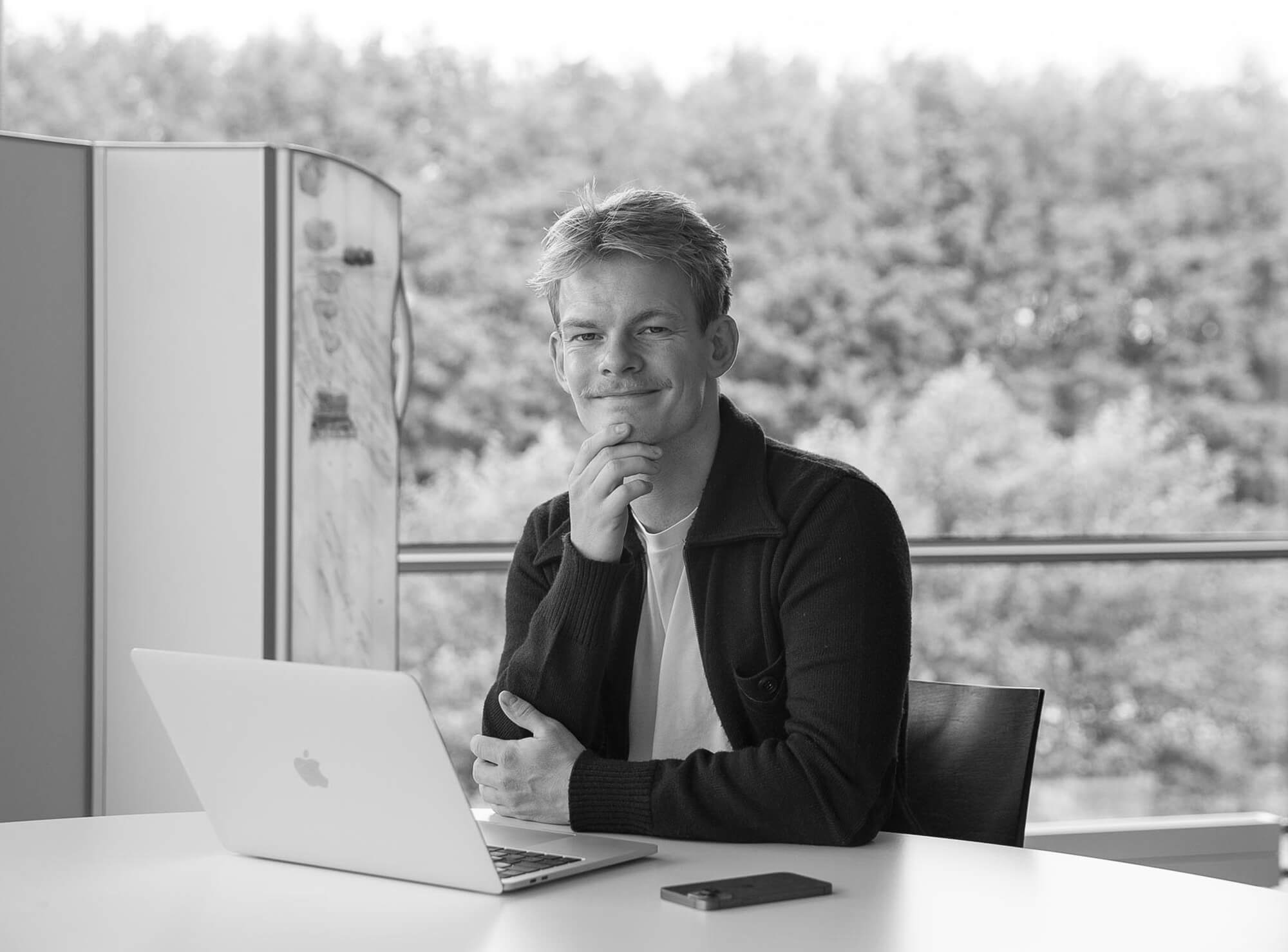 Zwart-witportret van Jonas aan zijn bureau met een laptop naast een Silentia-scherm, contactpersoon duurzaamheid.