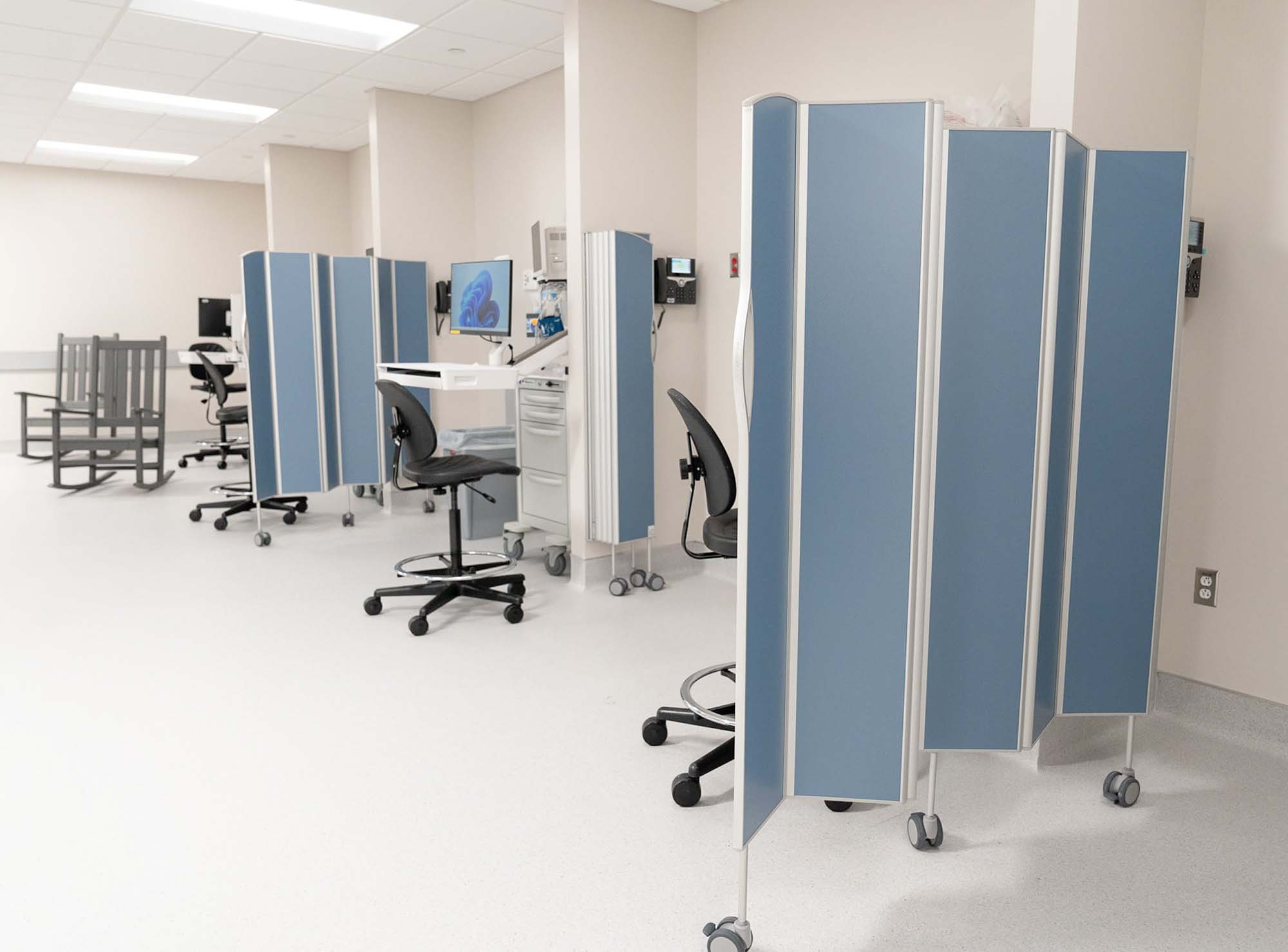 Behandlingsområde på klinik med arbetsstationer avdelade av blå mobila Silentia Fold-skärmar.
