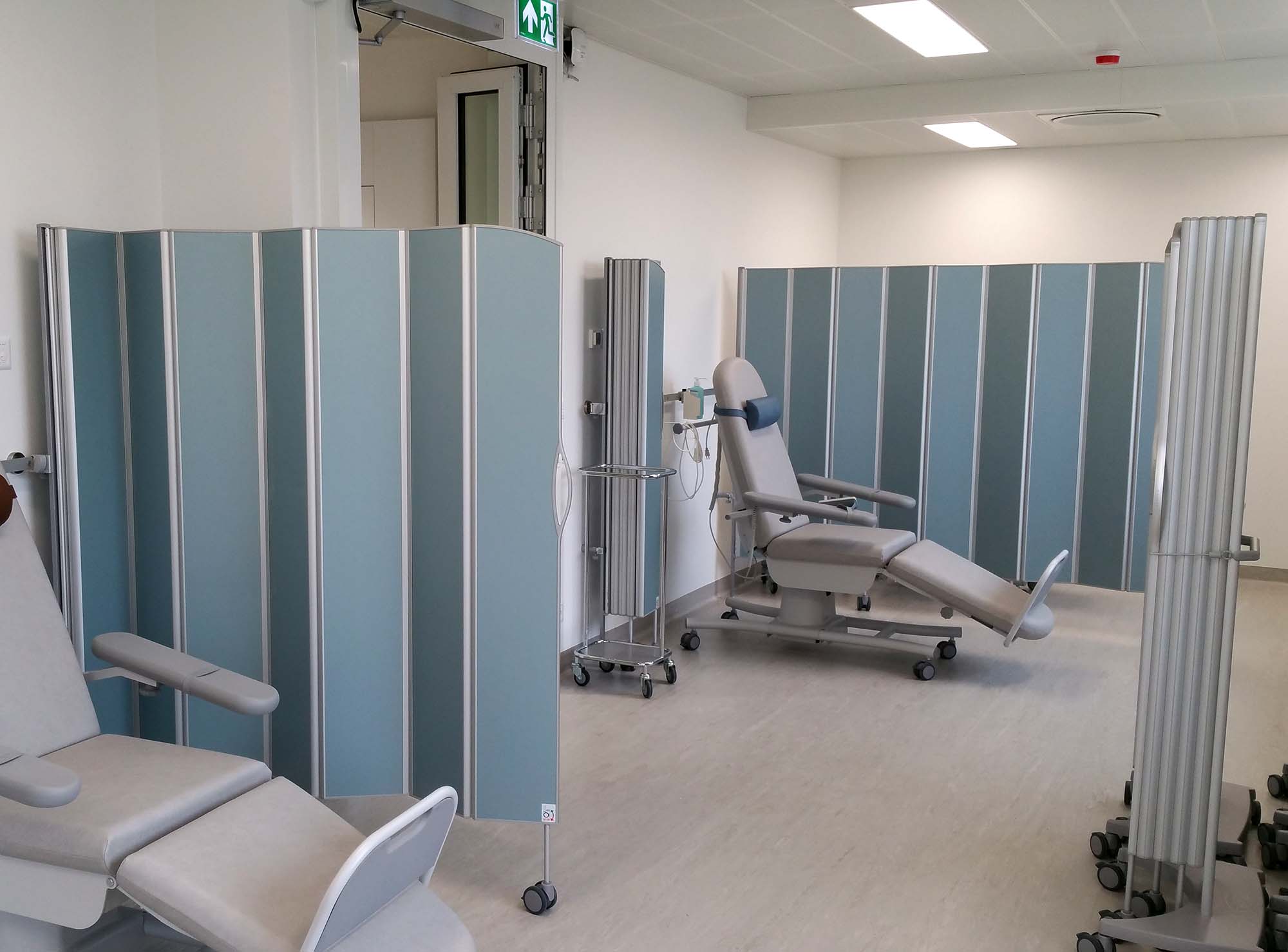 Behandlingsstolar i en klinik åtskilda av blå mobila Silentia Fold-skärmar.