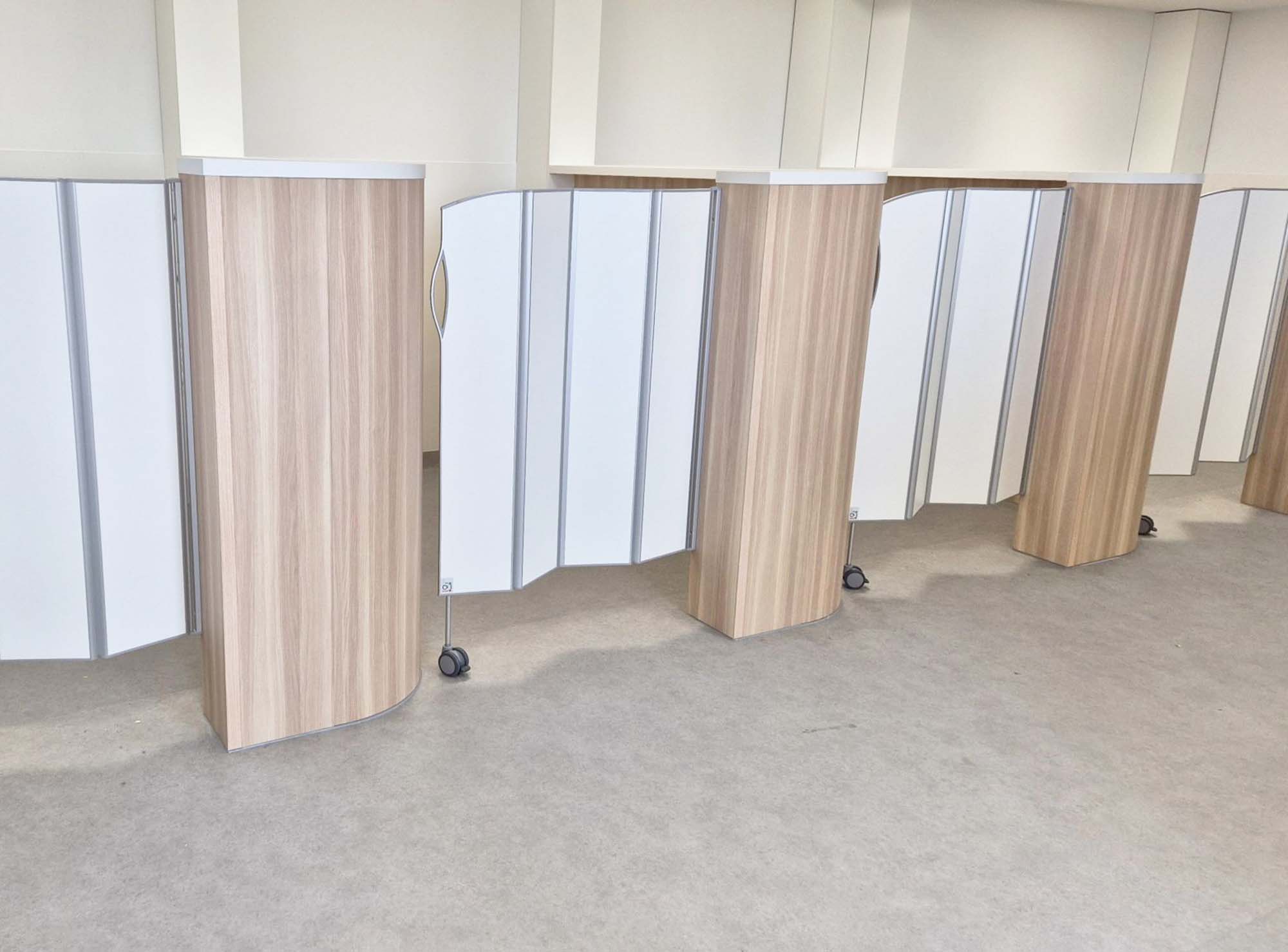 Behandlingsplatser avdelade av Silentia Fold-skärmar i vitt och träfanerlaminat.