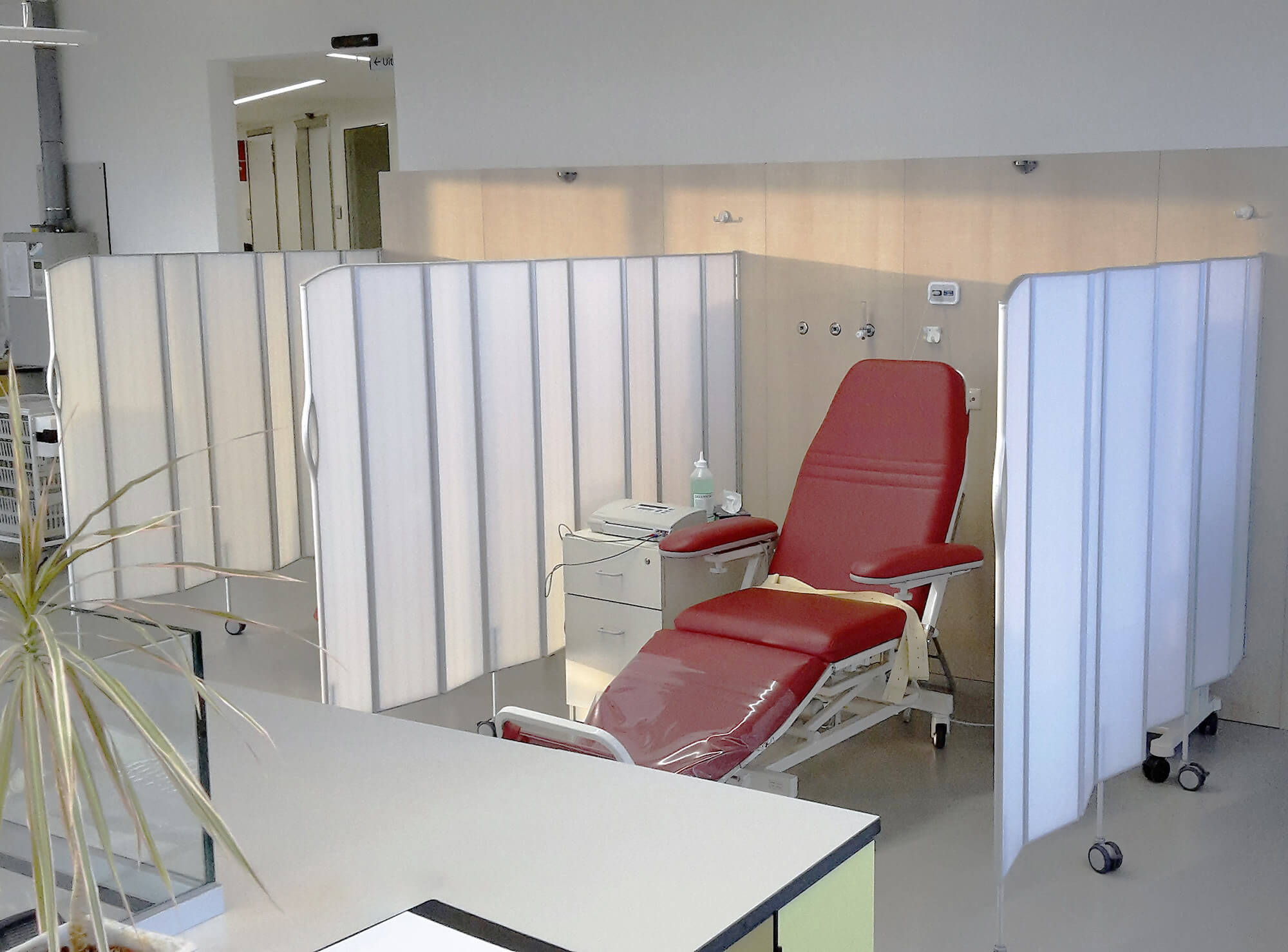 Behandlingsrum på klinik med en röd undersökningsstol avskärmad av vita Silentia Fold-skärmar.