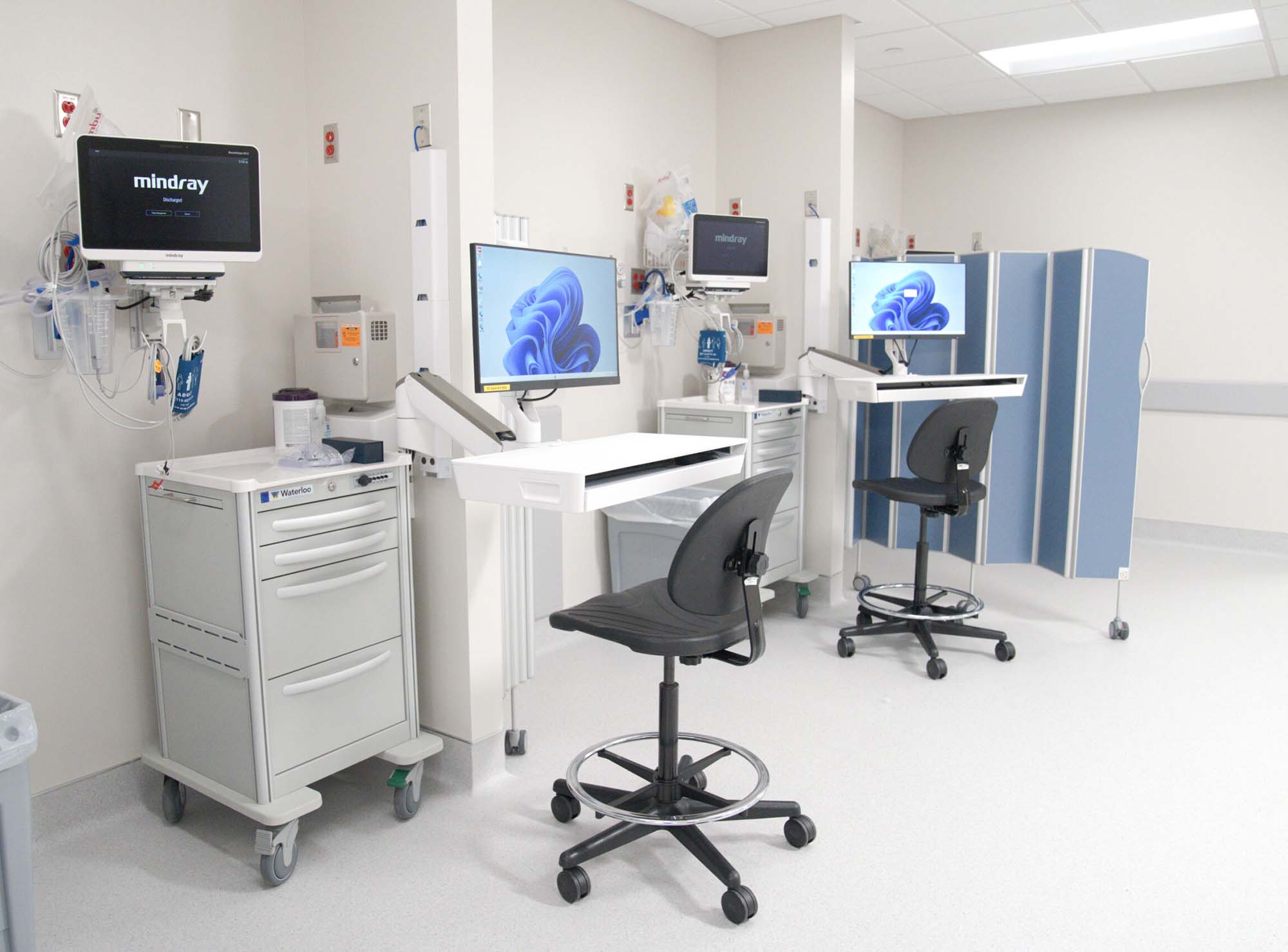 Blue Silentia Fold screen folded against the wall of a monitored-care bay with patient monitors and workstations.