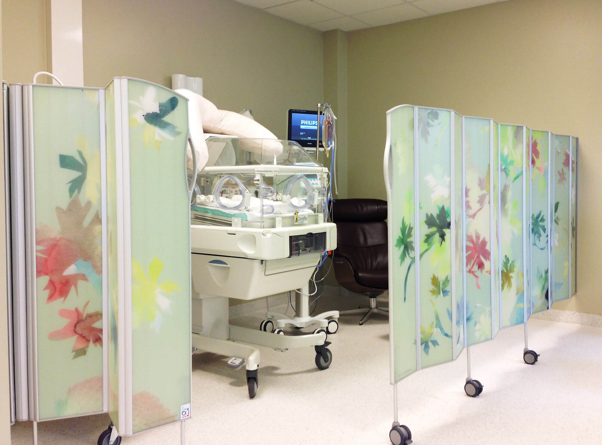 Silentia Fold screens with watercolour floral PhotoPanels™ enclosing an infant incubator in a neonatal room.