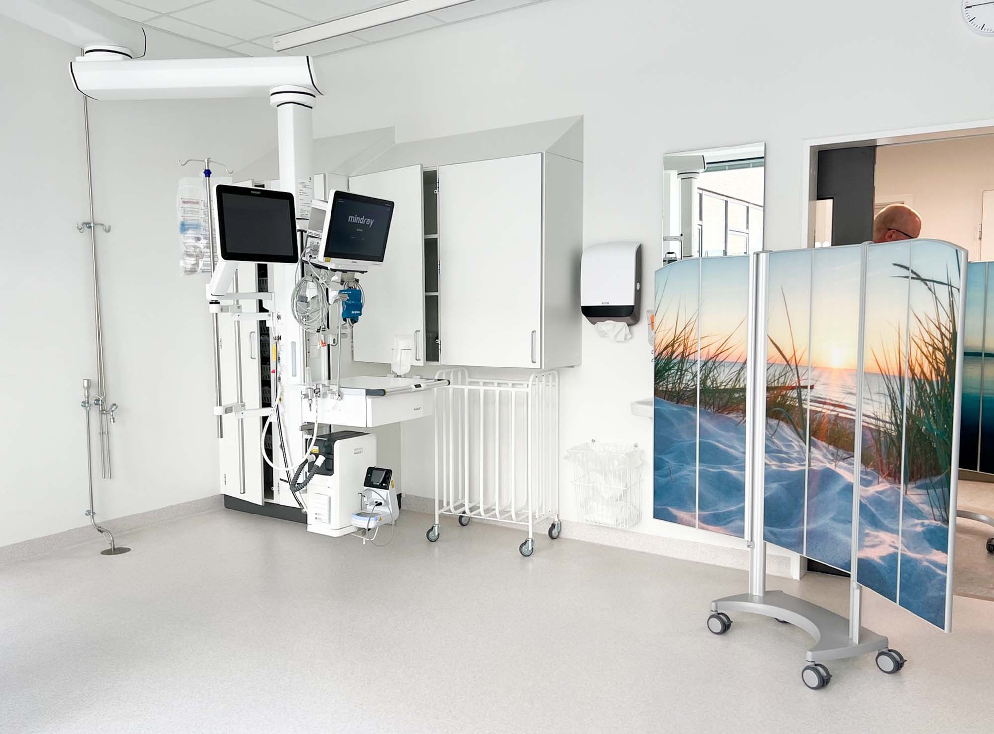 Silentia Fold screen with beach sunset PhotoPanels™ on a trolley shielding a monitored-care treatment bay.