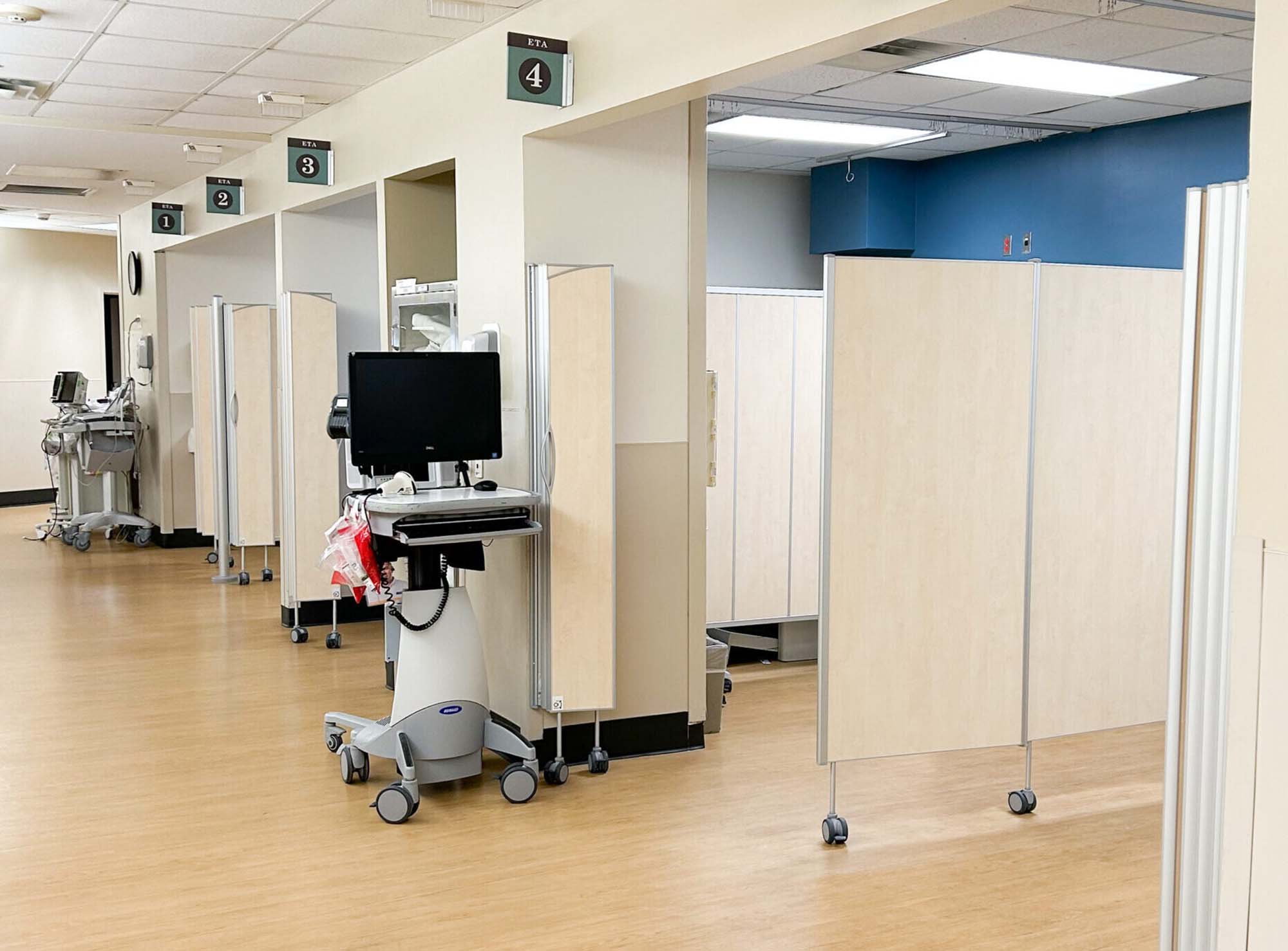 Birch-finish Silentia Fold screens forming numbered treatment bays along an open clinic corridor.