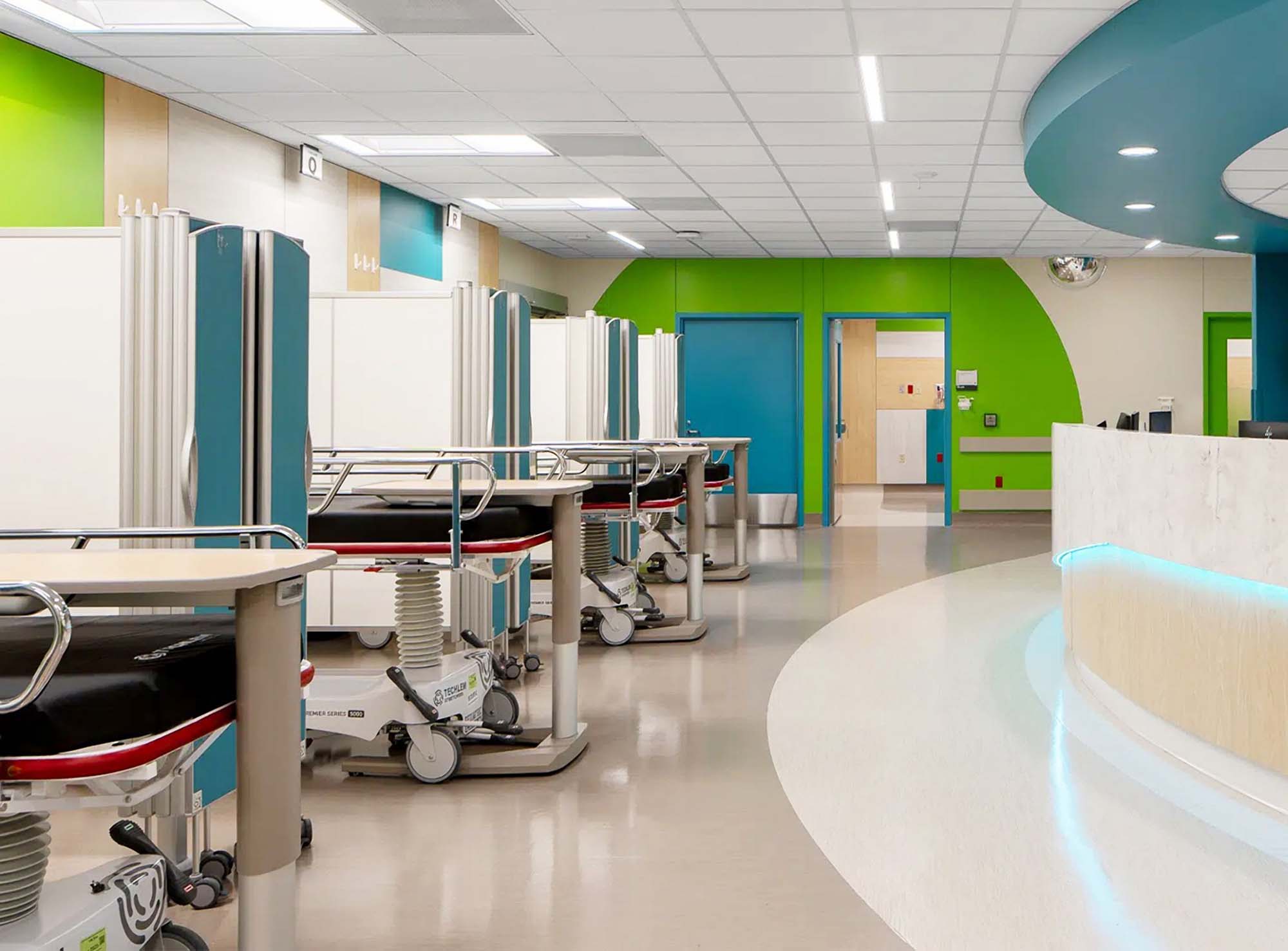 Blue Silentia Fold screens partitioning patient trolleys in a colorful open emergency care space.