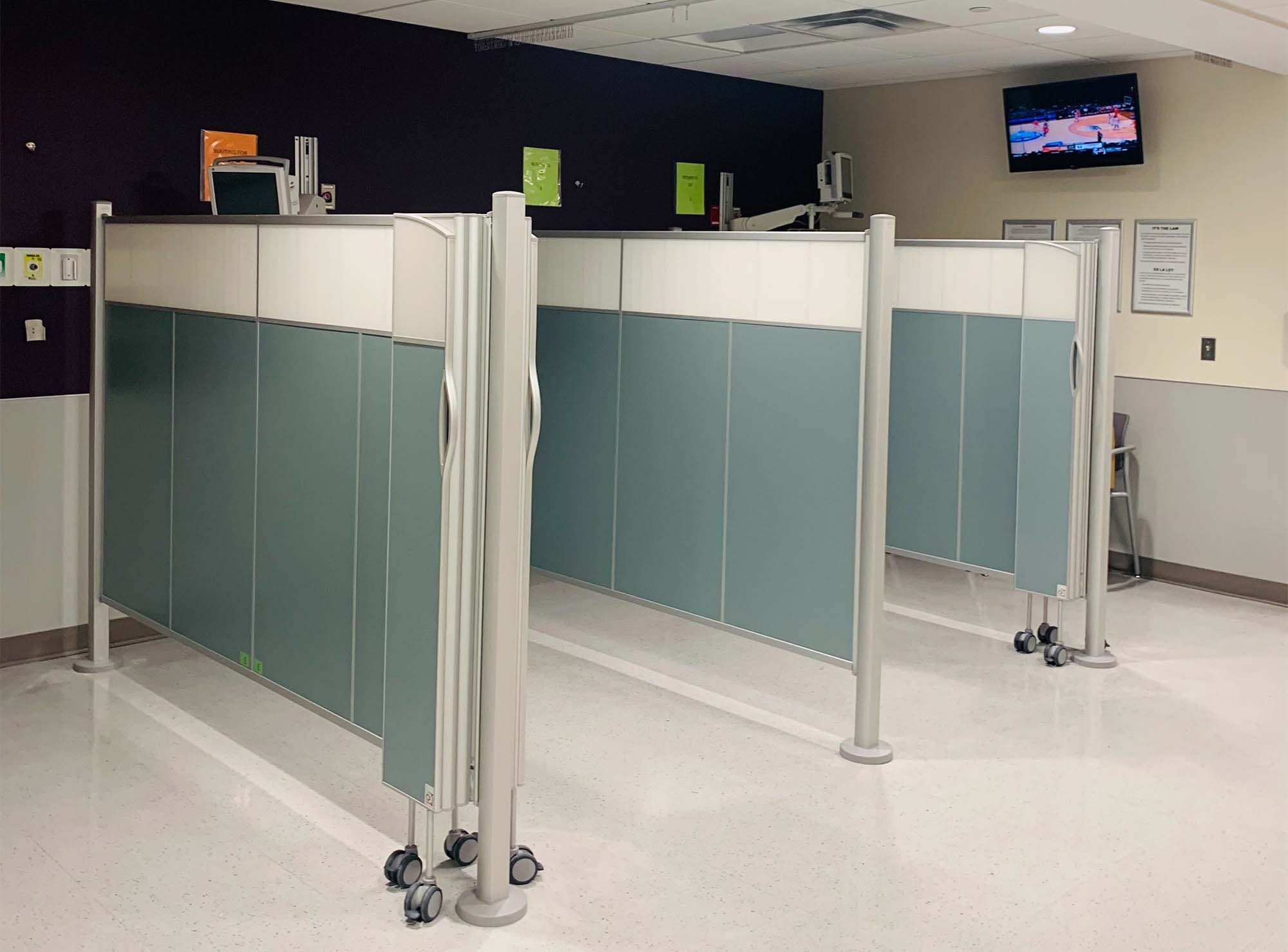 Green-gray Silentia Fixed screens on floor poles enclosing reception workstations in an open clinic.