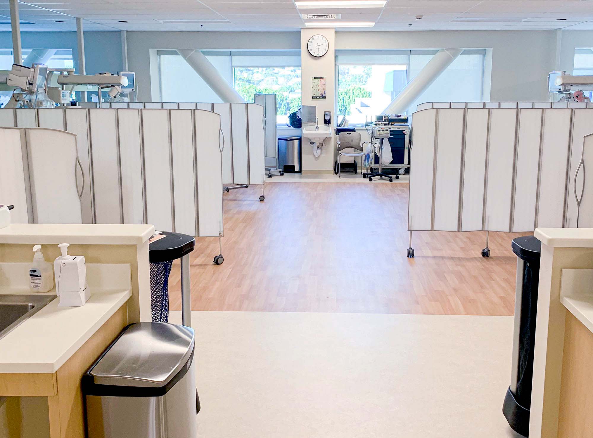 White Silentia Fold screens forming an open central walkway between care bays in a bright unit.