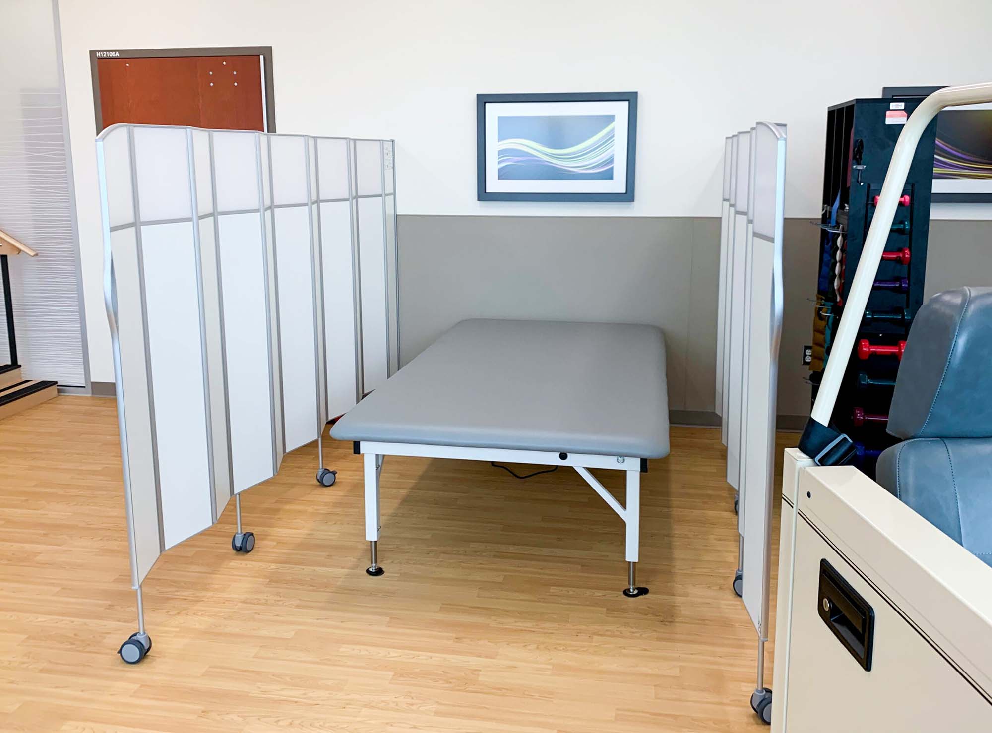 White Silentia Fold screens enclosing a treatment table in a physiotherapy and rehabilitation room.
