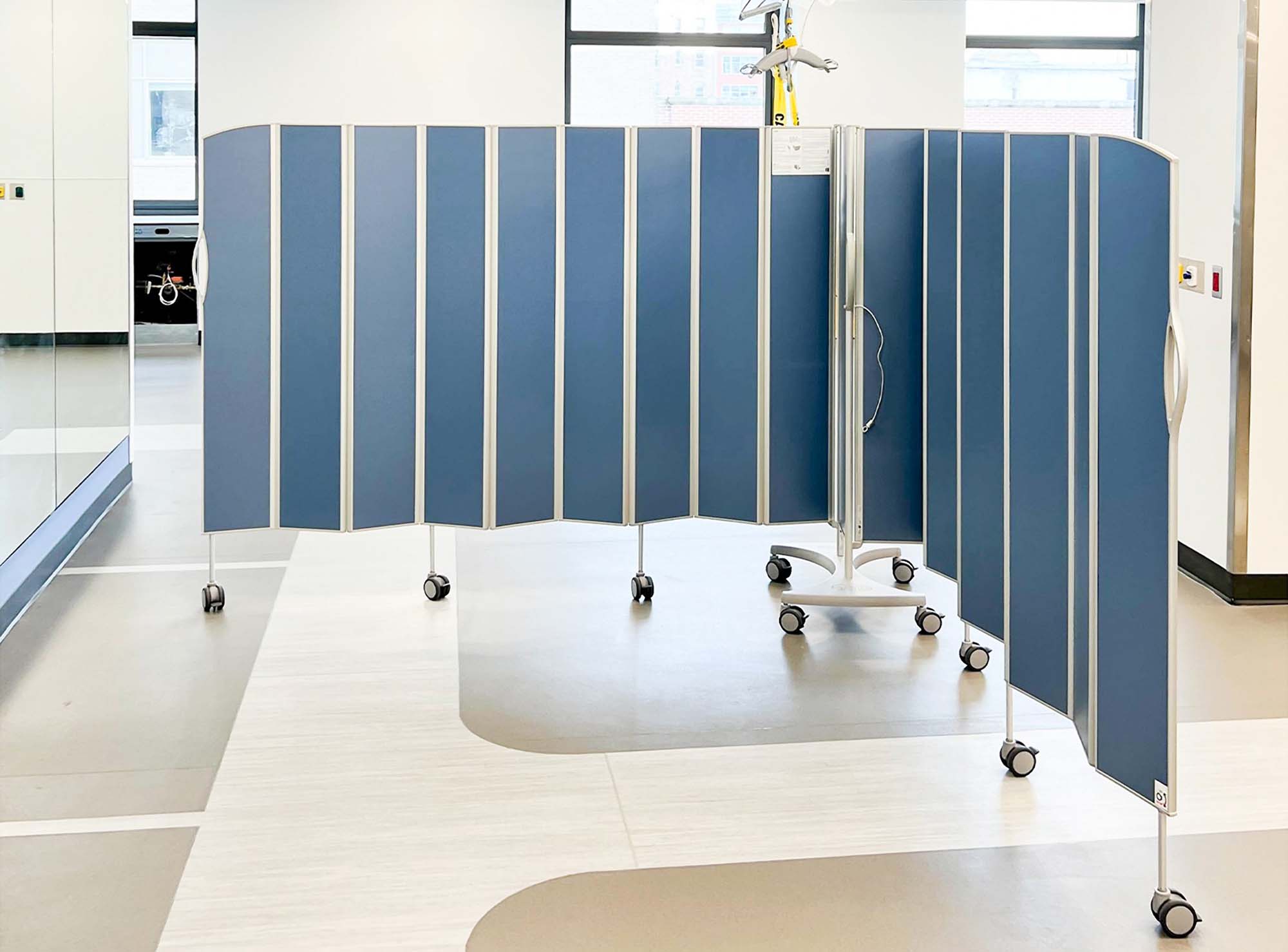 Blue Silentia Fold screens curved to enclose a private treatment area in a bright rehabilitation unit.