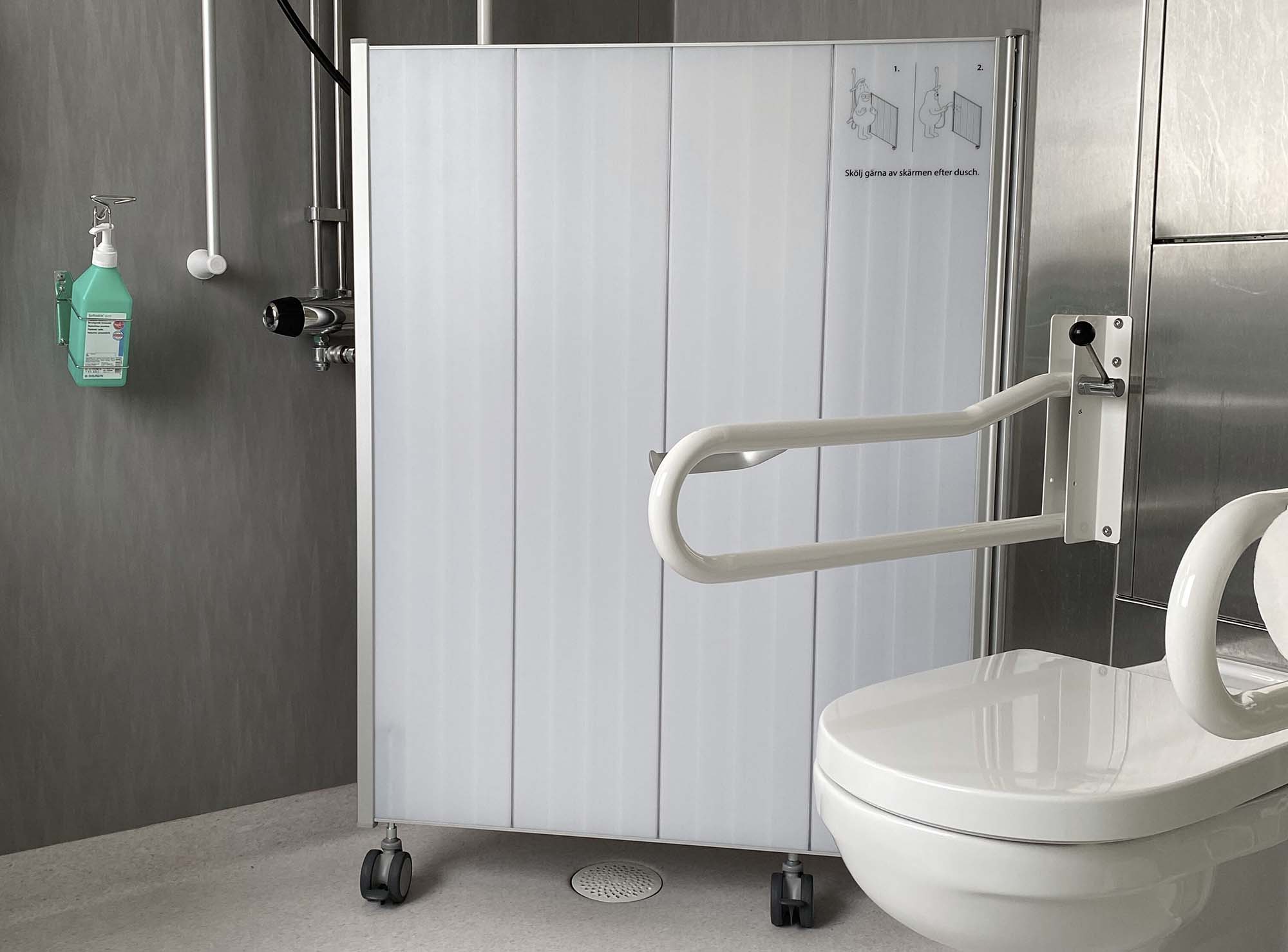 Mampara móvil Silentia Shower que resguarda un inodoro suspendido y una barra de apoyo en un baño accesible.