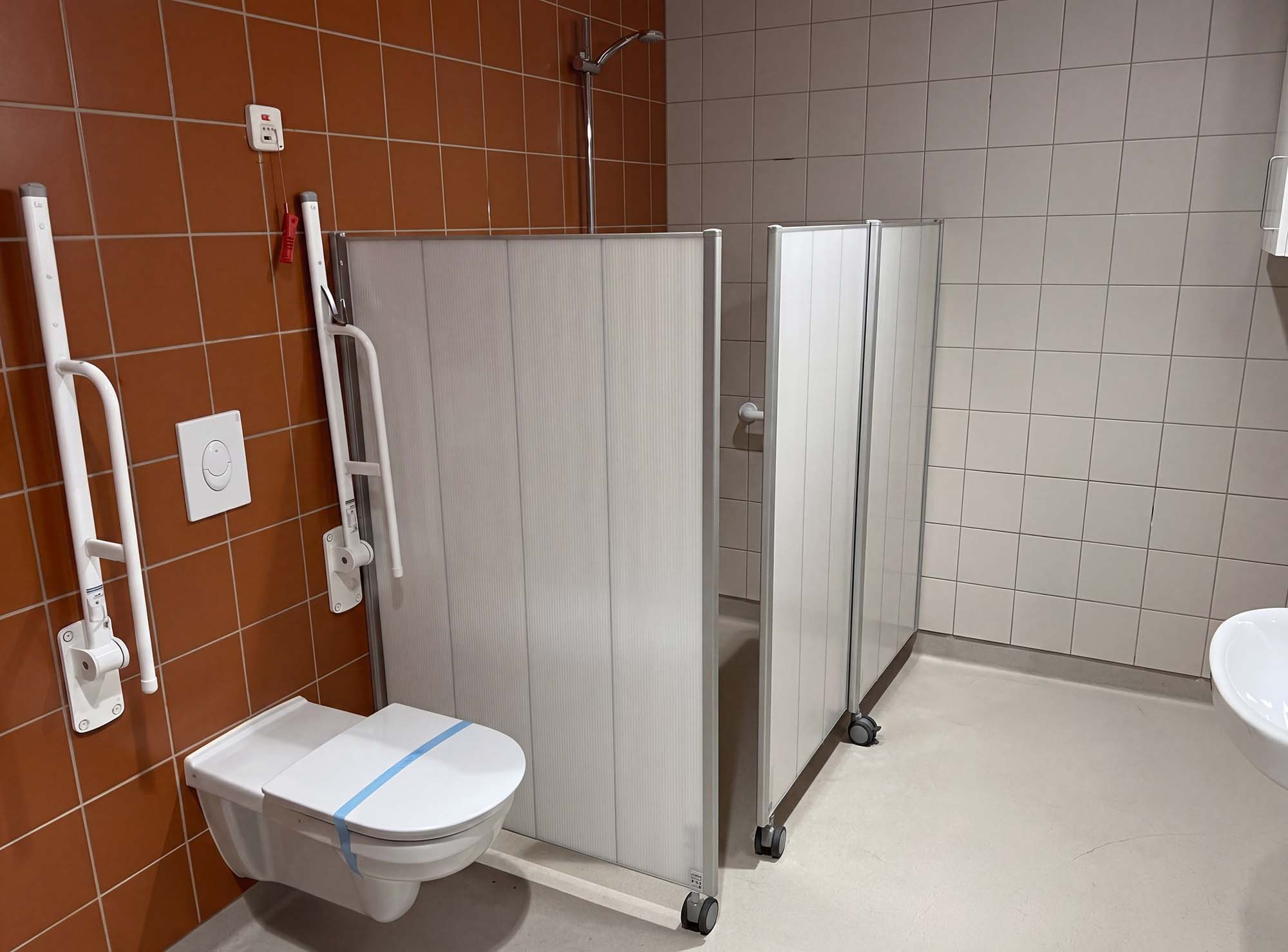 Dos mamparas Silentia Shower separan una ducha y un inodoro en un baño accesible.